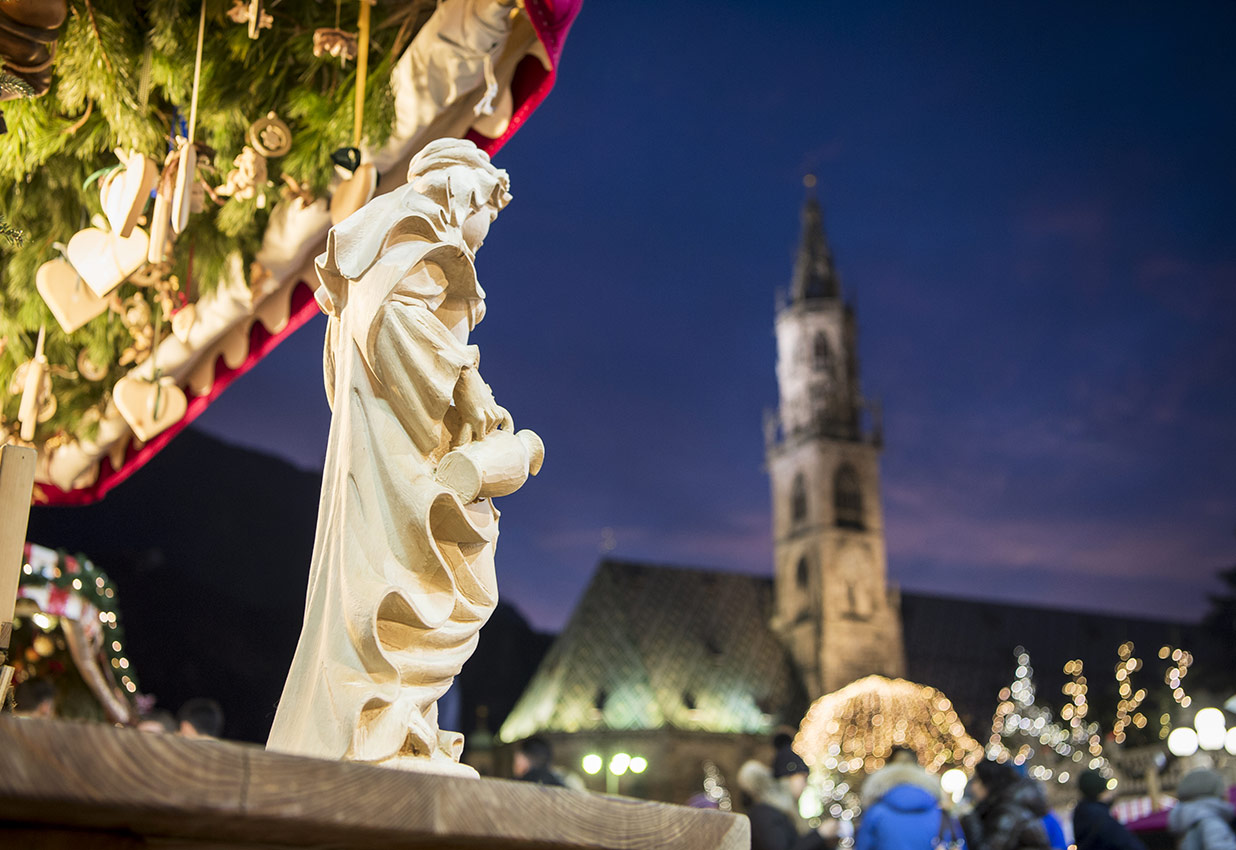 Dettaglio di una bancarella con sculture in legno e il Duomo sullo sfondo al Mercatino di Natale di Bolzano
